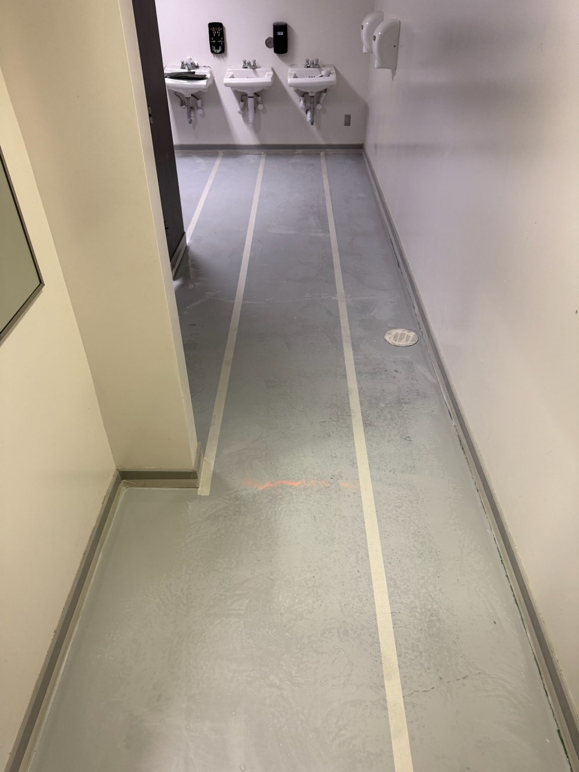 Commercial restroom epoxy floor installation in progress, with preparation lines around the sinks
